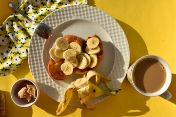French toasts with banana and cup of coffee with milk and small portion of peanut butter, top view