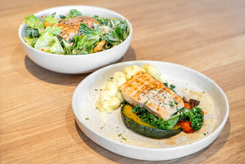 Tasty grilled salmon steak with mashed potatoes and vegetarian ceasar salad with grill steak salmon served on light wooden table.