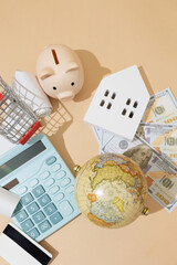 Top down close up view of symbolic economy objects: calculator, wooden house, bills, globe, piggy bank, and receipts representing an economic concept