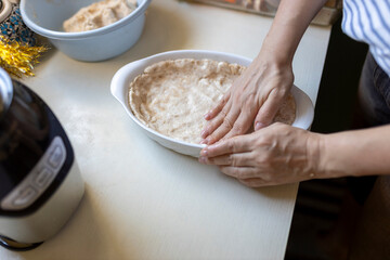 Close-up of a person's hands pressing pie crust dough into a white oval baking dish on a kitchen counter, preparing it for baking.