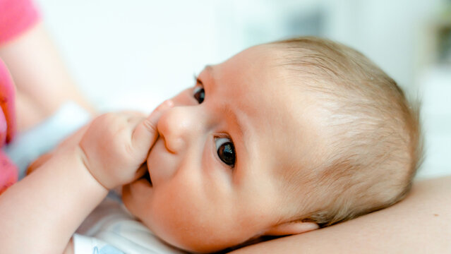 Baby at three months sucking thumb in parent's arms