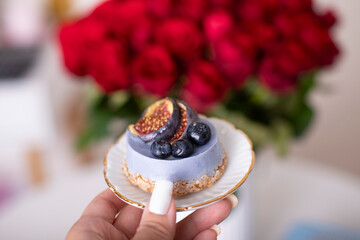 Female hand holding cake with fig and berries on rose background