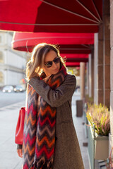 Young beautiful woman in grey coat and red scarf walking along the street