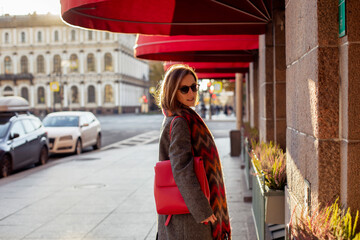 Young beautiful woman in grey coat and red scarf walking along the street