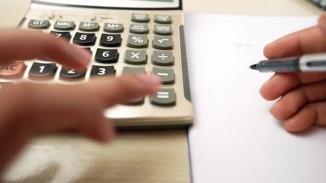 Close-up of hands using a calculator and writing on paper