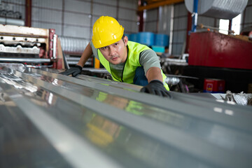 Construction worker inspecting steel sheets in industrial warehouse environment for safety and quality control