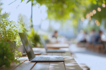 Outdoor coworking space with laptops on wooden table surrounded by green plants in natural daylight