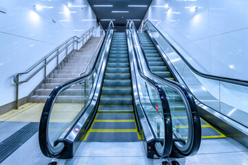 Wide symmetrical view of modern escalators in a subway or public transport station with cool blue...