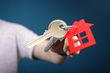 A person holds house keys with a red house tag. Concept of real estate, homeownership, and property...