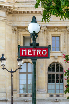 Vintage classic Paris Metro sign with ornate historic Parisian architecture in the background.