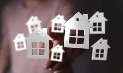 A hand holding and touching house icons. Illustrates concept of buying a home, property investment,...
