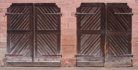 Zwei alte braune ländliche Holztore nebeneinander in einem Mauerwerk aus rotem Sandstein