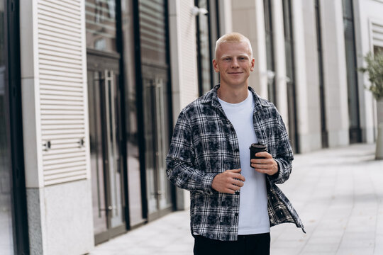 Young man with albino appearance holding coffee outdoors