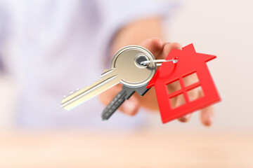 Person's hand holding house keys with a red house-shaped key tag. Represents home ownership, real estate, and new beginnings. Perfect for proper