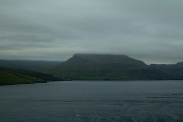 A stunning Faroe Islands landscape featuring calm waters surrounded by towering mountains, all shrouded in a mysterious blue mist, creating a tranquil and ethereal atmosphere.