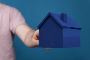 A person's hand holding a blue house model, symbolizing real estate, property, home ownership, and the concept of housing. Ideal for illustratin