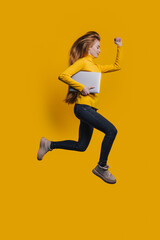 dynamic female sprinting holding her laptop, energetic woman in casual wear moving swiftly