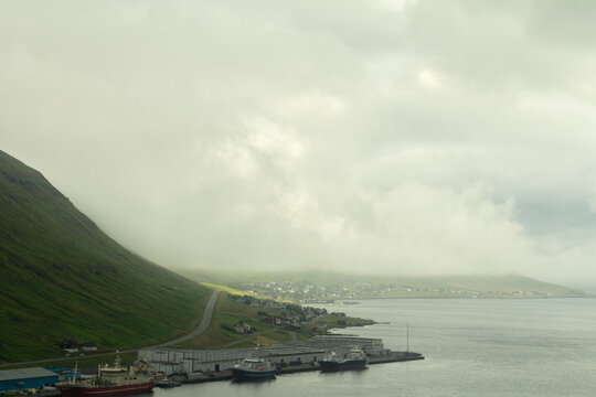 Faroese cityscape with mountain peaks covered in clouds and calm water in the foreground, showing the mix of nature and Nordic urban life.