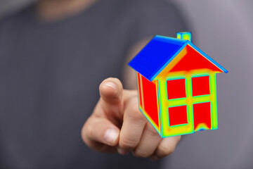 Close-up shot of a hand pointing towards a colorful 3D house model. Concept for energy efficiency, real estate, and home construction. Includes