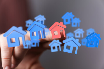 A hand touching 3D house models, symbolizing homeownership, investment, and the real estate market. Representing the dream of owning property an