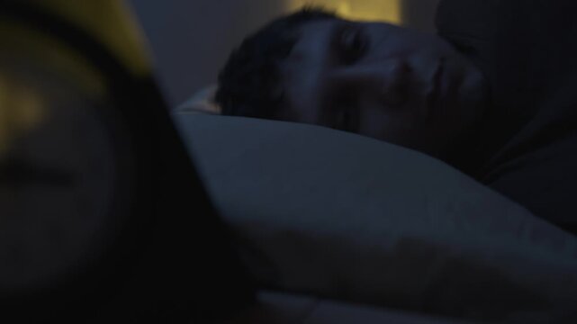 Man lying in bed suffering from insomnia night, sleepless bed and sleep deprivation, awake at midnight, close-up