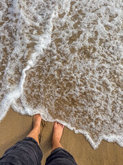 Feet on Sandy Beach with Ocean Waves Washing Ashore