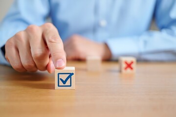 Hand selecting a wooden block with a blue check mark symbol cross decision