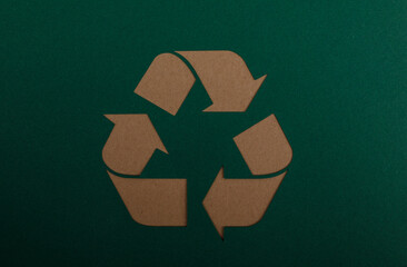 A close-up shot of a recycling symbol on a dark green background, representing environmental awareness, sustainability, and waste reduction. Ide