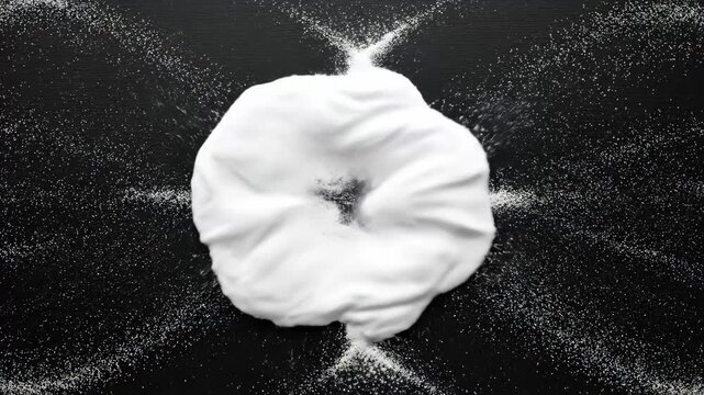Powder forming a decorative symmetrical pattern and a snowflake on a dark surface, design process time lapse footage.