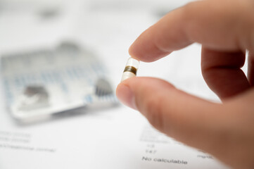 Hand holding a capsule medication over medical documents