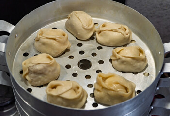 Delicious Manty, posture, khinkali is prepared in a special pot - mantoverde. Dishes of Asian, Buryat, Georgian cuisine. Aluminum steamer for cooking mantas on a stove in a home kitchen. Meat food.