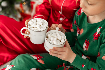 Close up hands of young woman in red pajamas and her little son at home near a Christmas tree, hold...