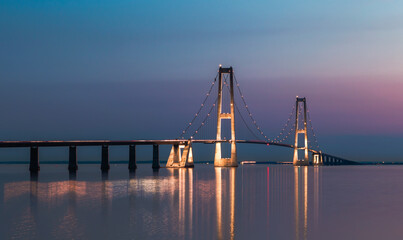 Fototapeta premium Illuminated Great Belt Bridge Reflected in Water at Night or Blue Hour