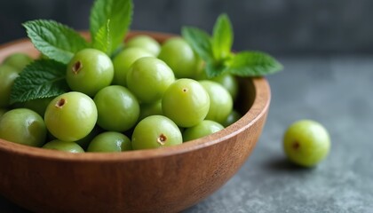 Fresh green gooseberries in wooden bowl with mint leaves. Ripe berries with water drops are a healthy, organic ingredient for cooking and desserts. They offer a tart and sweet taste.