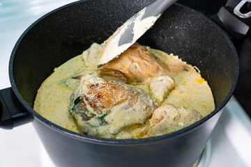 Chicken pieces simmering in a creamy herb sauce in a black pot