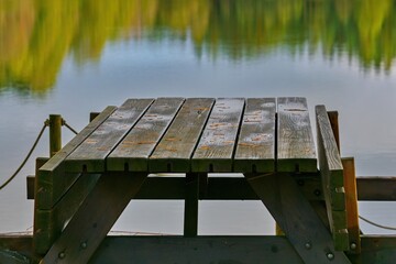Fototapeta premium A wooden pier table by a calm lake with reflections of an autumn forest, perfect for a peaceful outdoor scene.