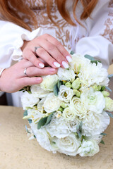Wedding bouquet with wedding rings and hands of the newlyweds.