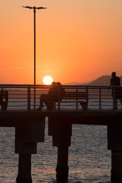 Santos city, Brazil. Colorful sunset at Fishermen's Deck. Silhouette of a couple enjoying the view alongside a fisherman.