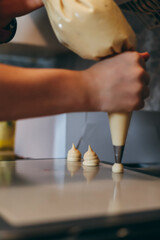 Pastry chef piping choux dough on baking tray in kitchen