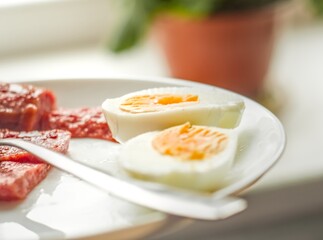 Sliced boiled eggs and cured meat arranged on a white plate - Two halves of boiled eggs with bright yolks and slices of sausages