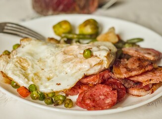 High-protein breakfast plate with fried egg, bacon, sausage, and peas