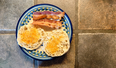 toasted english muffin with orange jam and two strips of bacon on a painted blue plate 