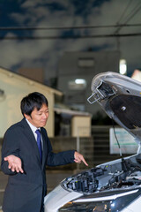 車のボンネットを開けてお手上げのスーツの男性