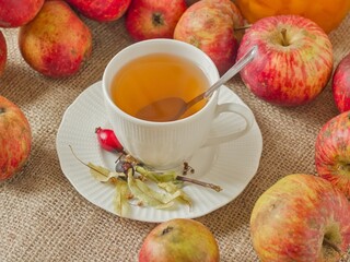 A white cup of linden tea with a spoon, set against a backdrop of fresh autumn apples