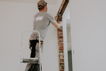 A young Caucasian male builder clears a doorway using a crowbar.
