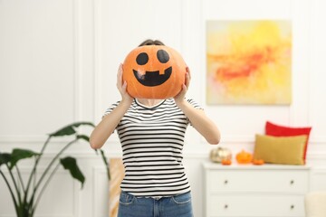 Happy Halloween. Woman hiding behind pumpkin with face drawing at home