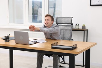 Young businessman stretching his arms at table in office