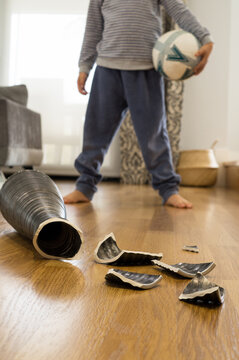 Out-of-focus child with a ball under his arm in front of a vase he has just broken