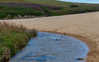 A scenic landscape image shows a stream running along a sandy beach. In the background  in Holywell Bay - Cornwall - UK