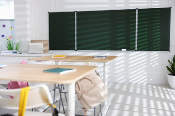 Green chalkboard, desks and chairs with backpacks in classroom